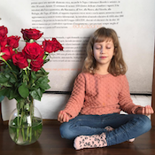 Bambina che medita con le gambe incrociate accanto a un vaso di vetro pieno di rose rosse